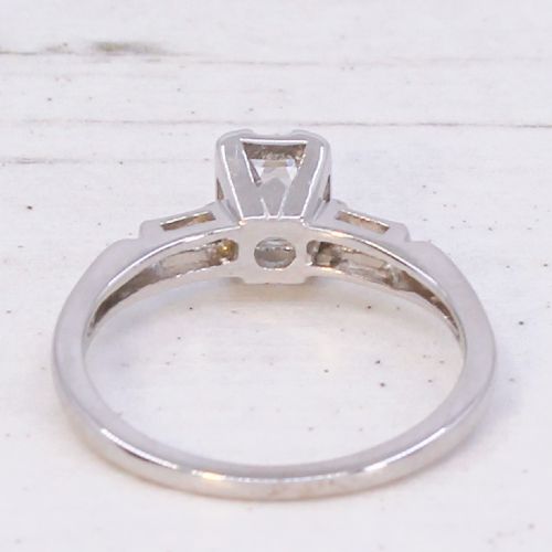 A silver-toned metal ring featuring a central rectangular emerald-cut diamond flanked by two baguette-cut diamonds on the shoulders. View V