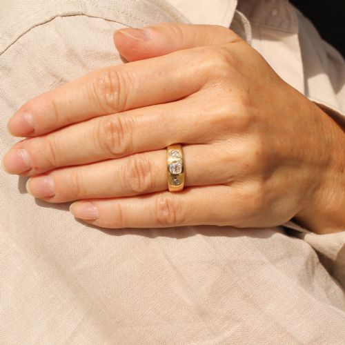 fig 1. A smooth yellow gold wide band ring featuring three flush-set old cut diamonds across the front.