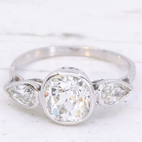 fig 2. An Art Deco platinum ring featuring a central bezel-set old cushion-cut diamond flanked by two pear-cut side diamonds with milgrain edging.