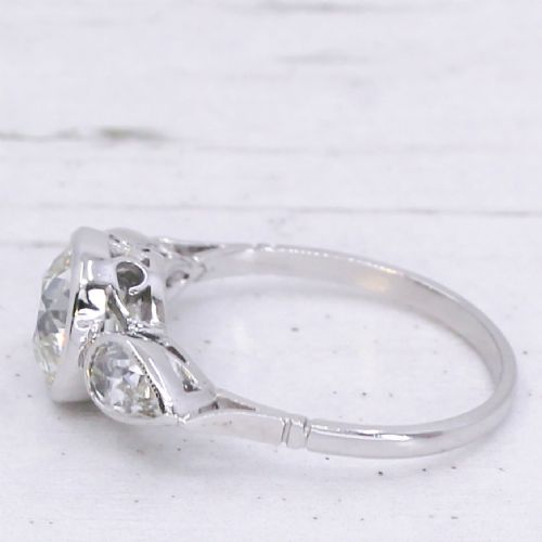 fig 3. An Art Deco platinum ring featuring a central bezel-set old cushion-cut diamond flanked by two pear-cut side diamonds with milgrain edging.