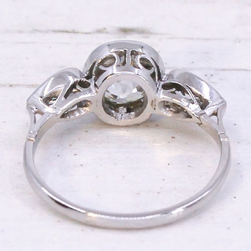 An Art Deco platinum ring featuring a central bezel-set old cushion-cut diamond flanked by two pear-cut side diamonds with milgrain edging. View V