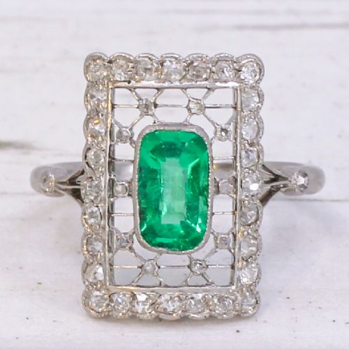 fig 2. An Edwardian rectangular platinum ring set with a central emerald-cut green gemstone framed by openwork filigree and a diamond border.