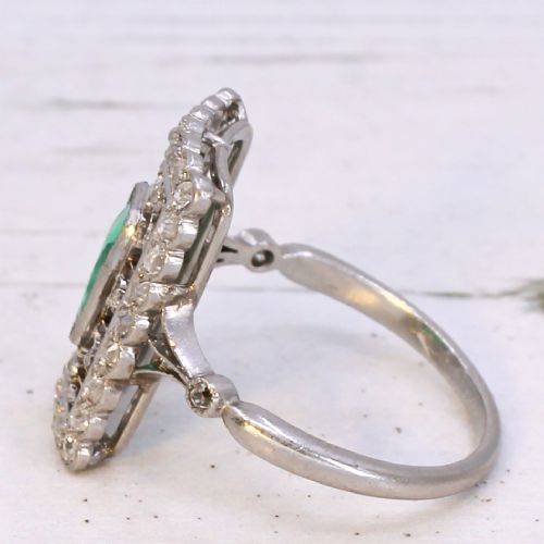 fig 3. An Edwardian rectangular platinum ring set with a central emerald-cut green gemstone framed by openwork filigree and a diamond border.