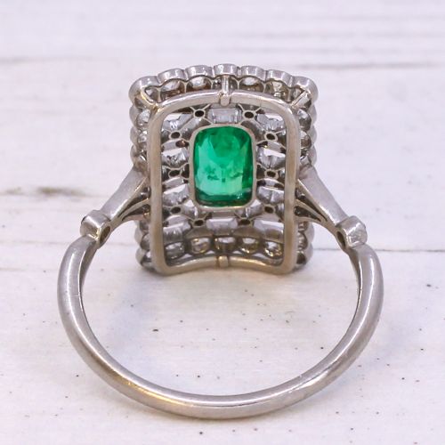 fig 4. An Edwardian rectangular platinum ring set with a central emerald-cut green gemstone framed by openwork filigree and a diamond border.