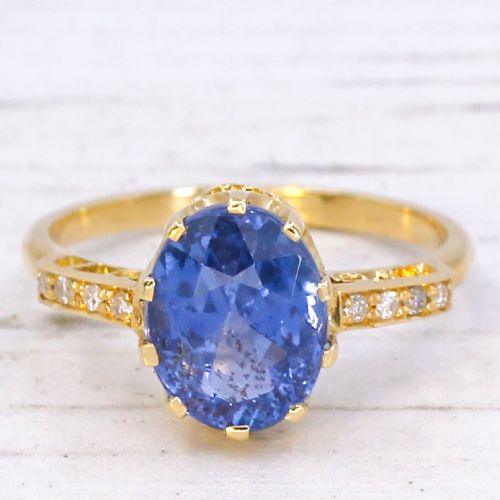 fig 2. A vintage yellow gold ring featuring an oval-cut blue sapphire in a claw setting with diamond-set shoulders.