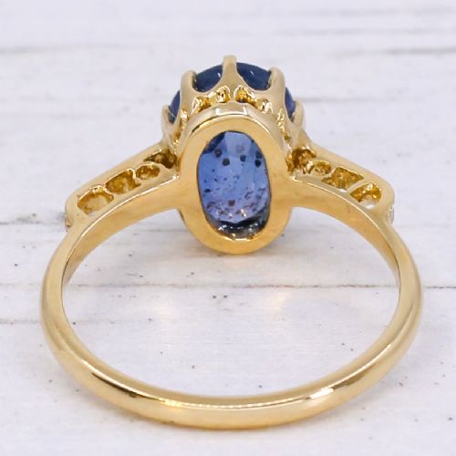 fig 4. A vintage yellow gold ring featuring an oval-cut blue sapphire in a claw setting with diamond-set shoulders.