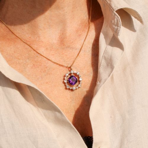 fig 1. An antique yellow gold pendant featuring a central cushion-cut purple amethyst encircled by an openwork gold border and a halo of old-cut diamonds.