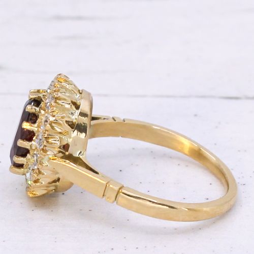 fig 3. A vintage yellow gold ring featuring a central oval-cut red ruby framed by a halo of brilliant round diamonds.