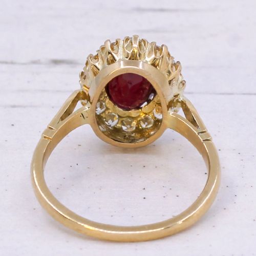 A vintage yellow gold ring featuring a central oval-cut red ruby framed by a halo of brilliant round diamonds. View V