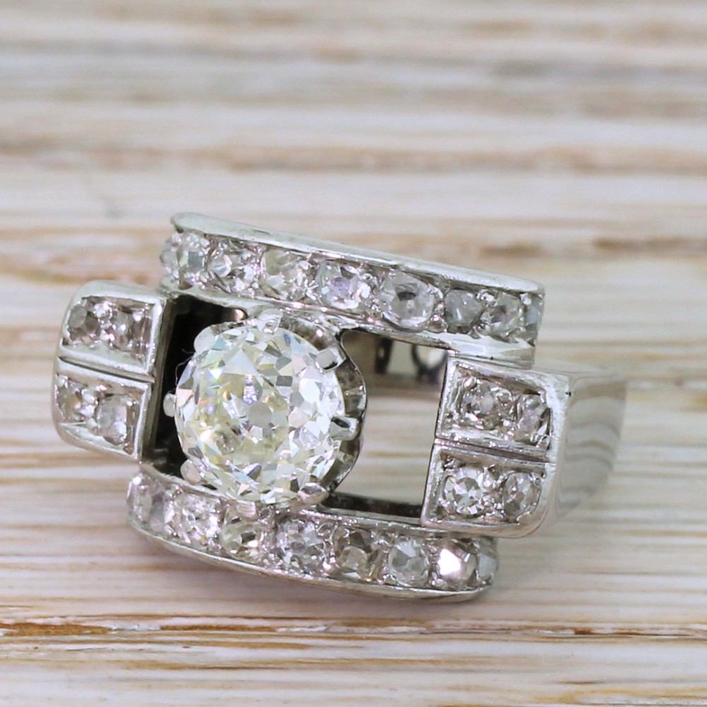 An Art Deco diamond ring featuring a central round old European cut diamond set within an architectural rectangular metal frame surrounded by accent diamonds.