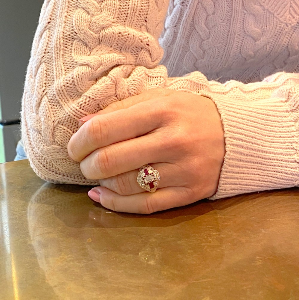 A retro silver-tone ring featuring a central emerald-cut diamond flanked by two rectangular rubies surrounded by pierced filigree work. View VIII