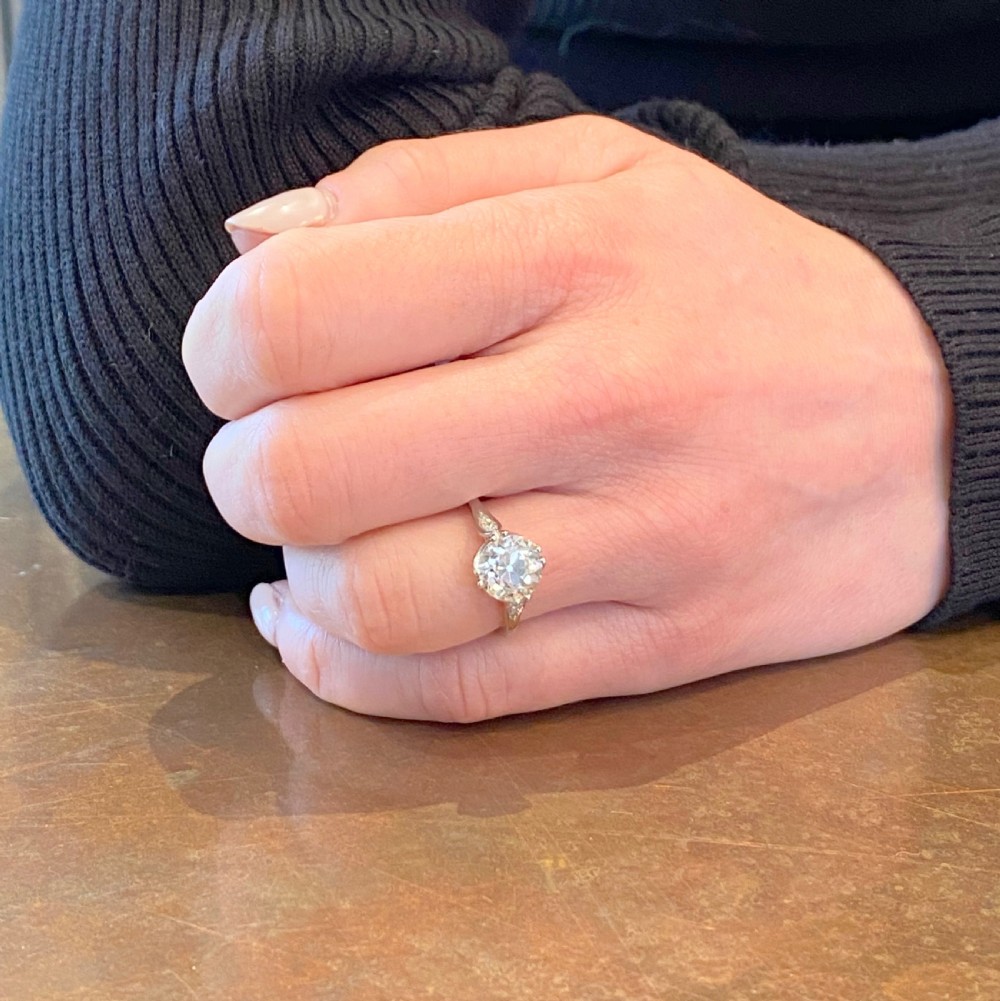 An Art Deco platinum solitaire ring set with a central old cut diamond and accent diamonds set into carved shoulders. View VII