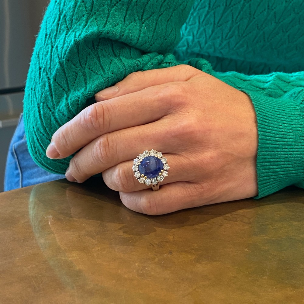 A mid-century cluster ring featuring a central oval blue sapphire surrounded by round brilliant and baguette diamonds set in platinum. View VIII