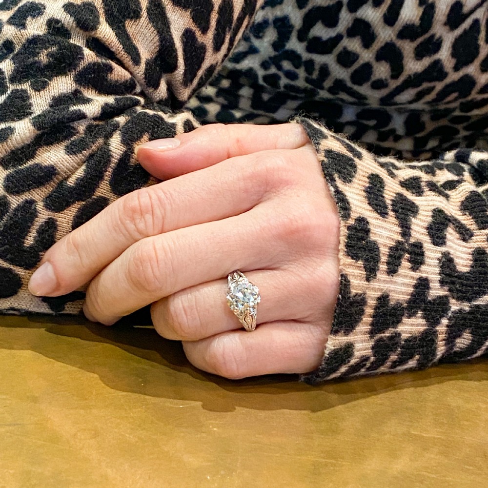 A mid-century solitaire ring featuring a central round old-cut diamond set in a multi-claw platinum mounting with carved foliate shoulder details. View VIII