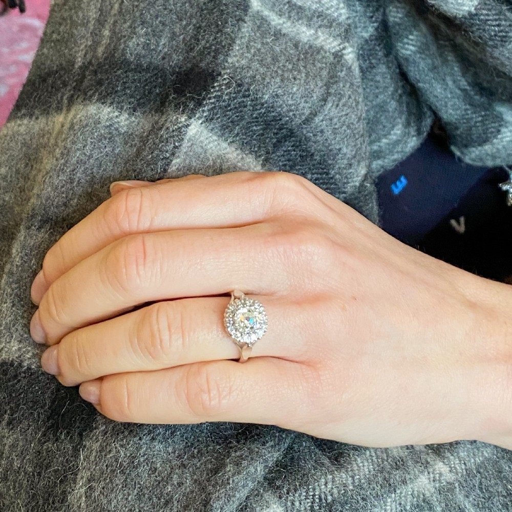 An Art Deco style white metal ring featuring a central round diamond surrounded by a halo of smaller diamonds on a carved shoulder band. View VIII