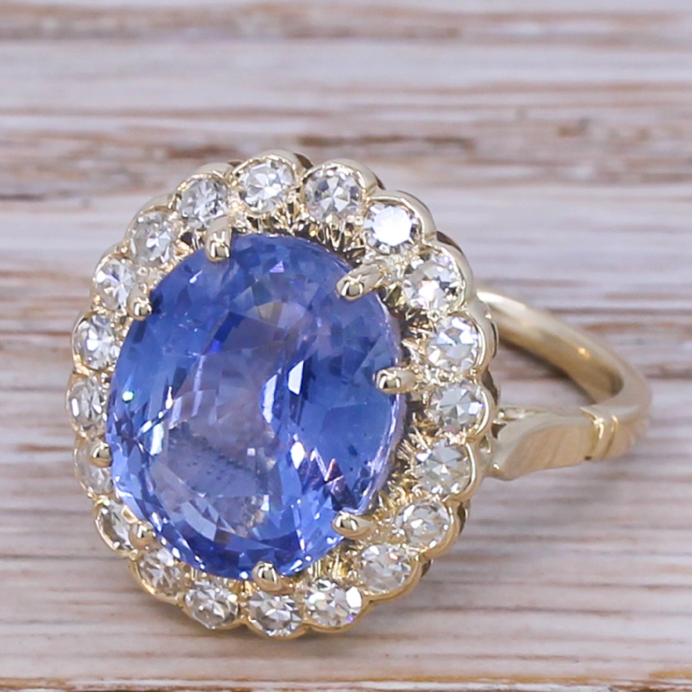 An Art Deco cluster ring featuring a large oval Ceylon sapphire surrounded by a halo of round diamonds mounted on a gold band.