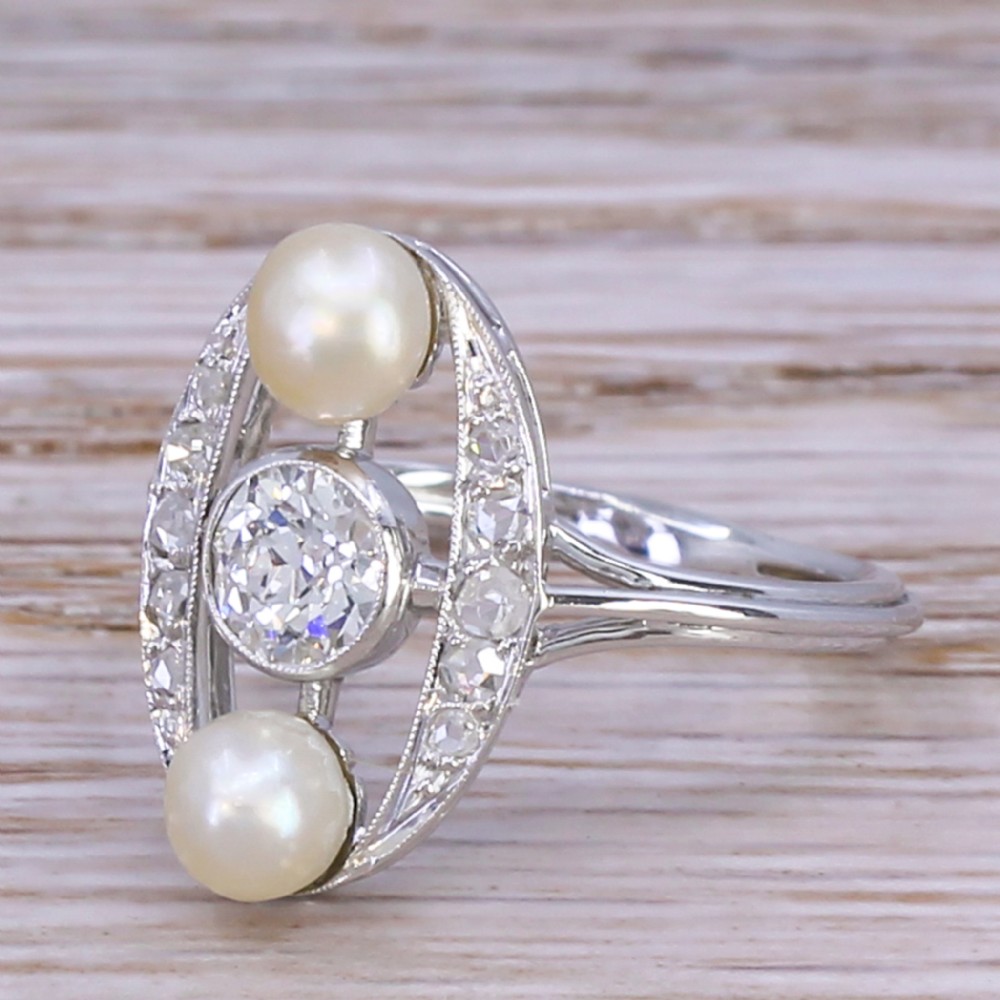 A mid-century platinum dress ring featuring a central bezel-set round diamond flanked vertically by two white pearls inside an openwork oval diamond-set frame.