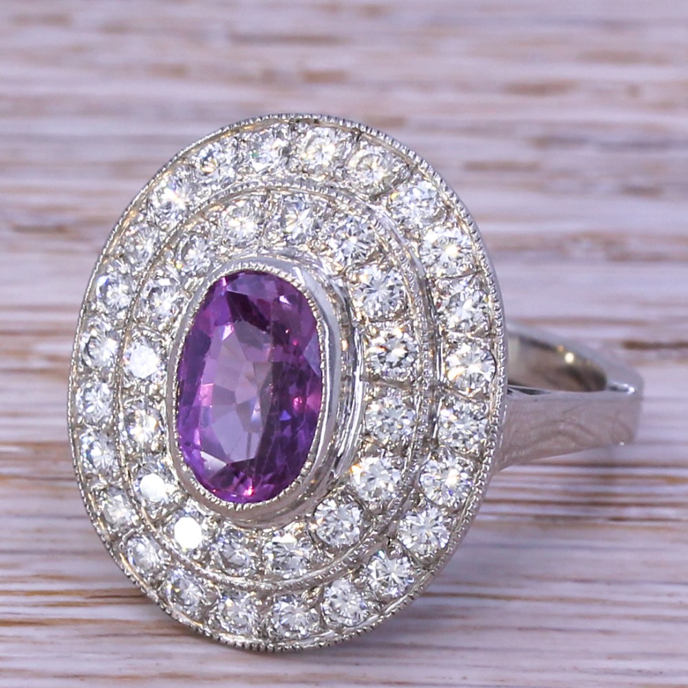 An oval purple sapphire mounted within a double halo of brilliant-cut diamonds on a platinum ring band.