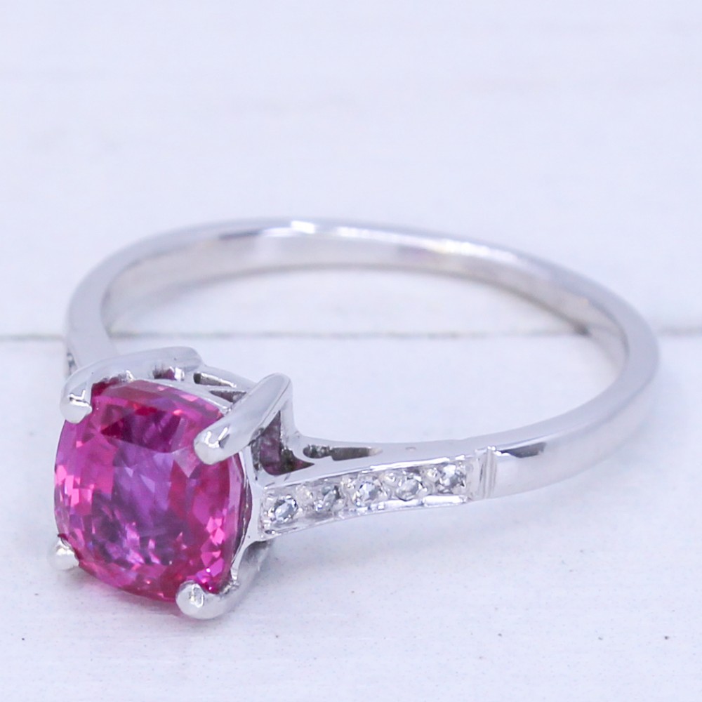 A mid-century platinum solitaire ring featuring a central cushion-cut pink sapphire with small accent diamonds set into the shoulders.