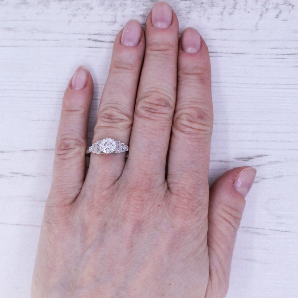 An Art Deco platinum engagement ring featuring a central round old European cut diamond flanked by geometric stepped shoulders set with accent diamonds. View VII