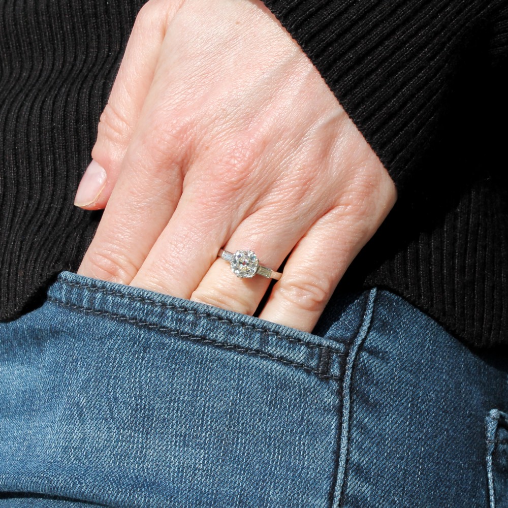 An Art Deco platinum engagement ring featuring a central round old cut diamond flanked by two rectangular baguette diamonds. View IV