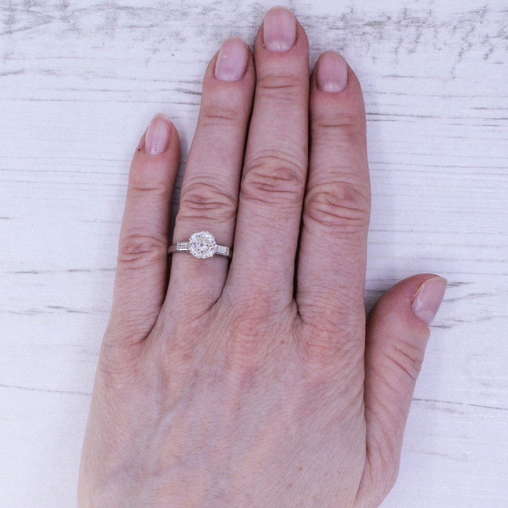 An Art Deco platinum engagement ring featuring a central round old cut diamond flanked by two rectangular baguette diamonds. View IX