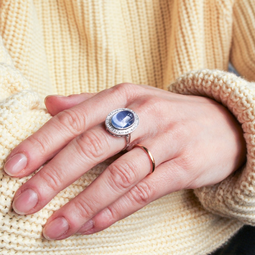 An Art Deco ring featuring a large oval cabochon blue sapphire surrounded by a platinum frame set with small diamonds. View VI