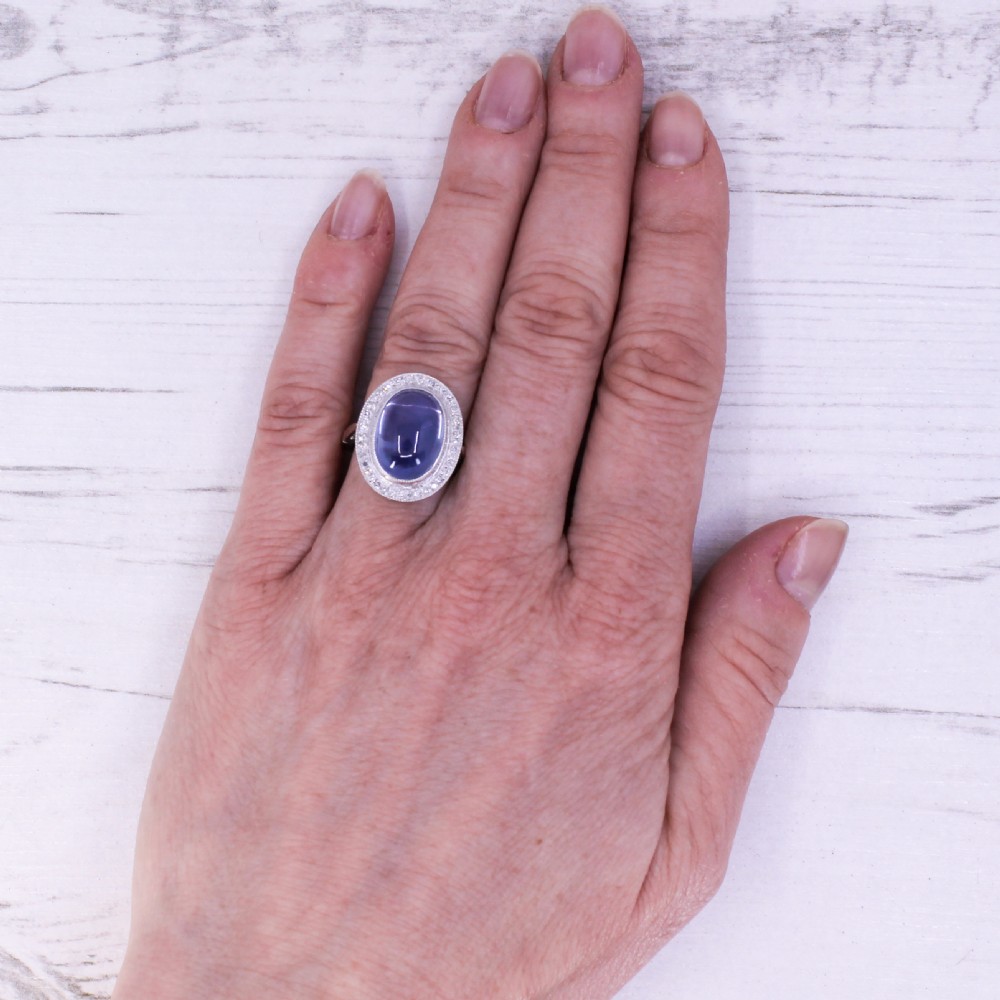 An Art Deco ring featuring a large oval cabochon blue sapphire surrounded by a platinum frame set with small diamonds. View VIII