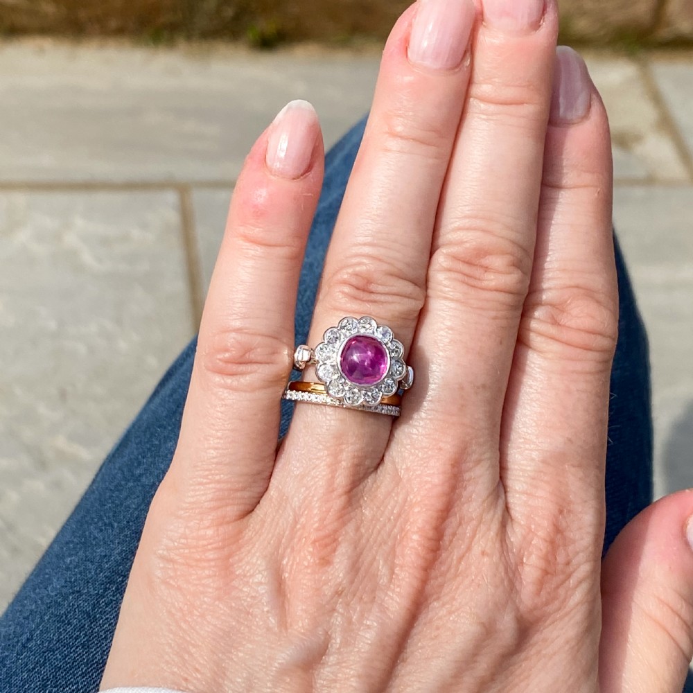 An Art Deco platinum ring featuring a central cabochon ruby surrounded by a cluster halo of round diamonds. View VI