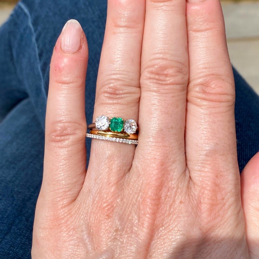 An Art Deco three-stone ring featuring a central square-cut green emerald flanked by two round diamonds on a platinum band. View VI