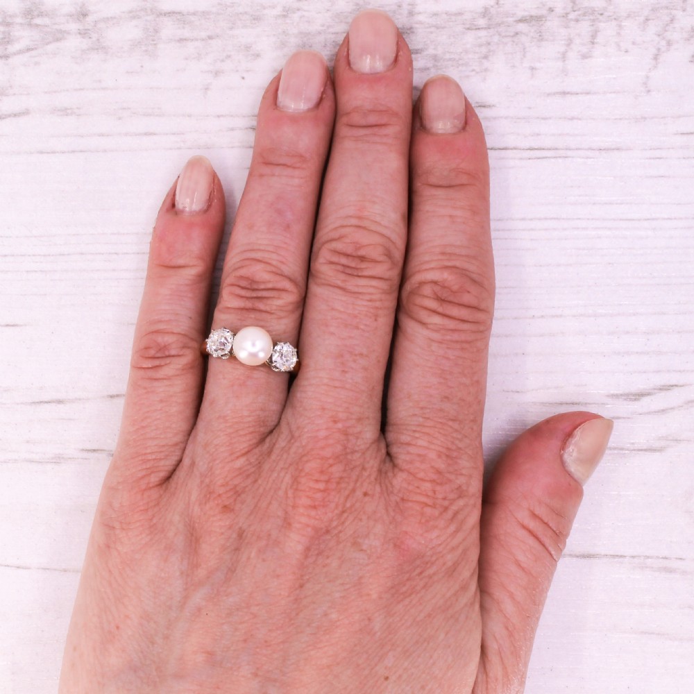 An Art Deco trilogy ring featuring a central white pearl flanked by two old cut diamonds on a gold shank. View VII
