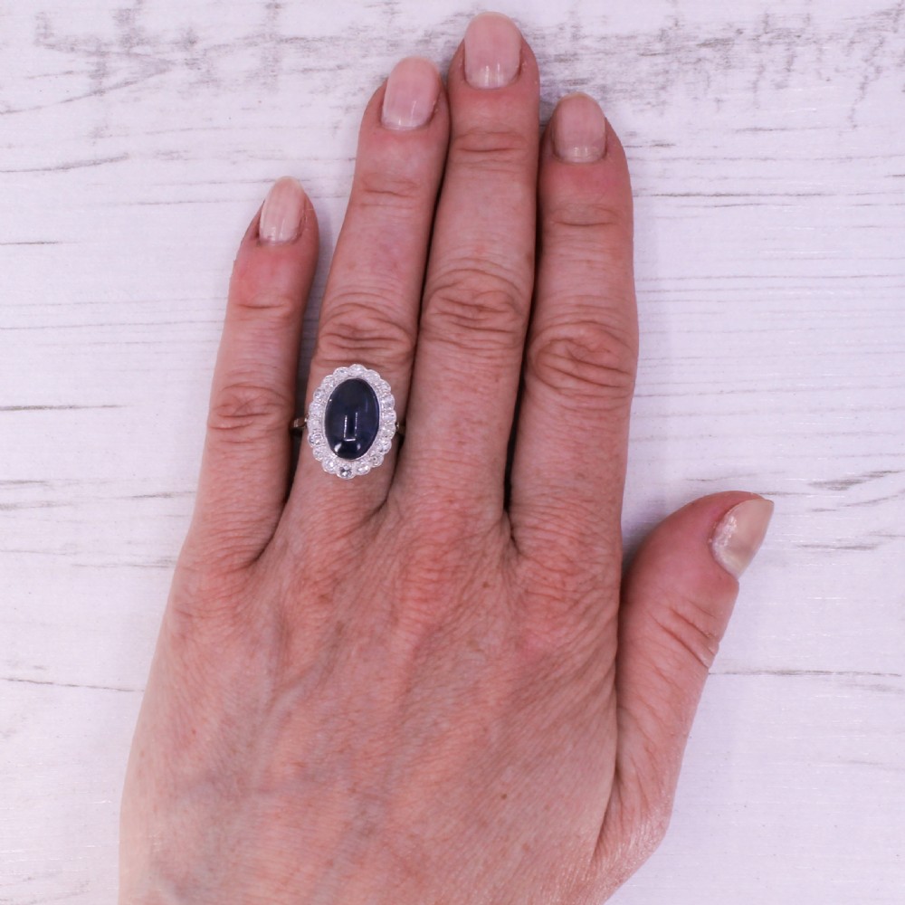 An Art Deco ring featuring an oval cabochon blue sapphire surrounded by a halo of diamonds set in a platinum band. View VII