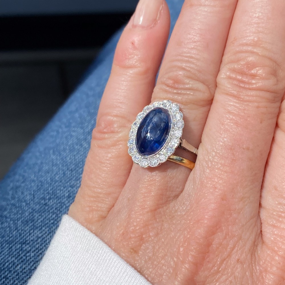 An Art Deco ring featuring an oval cabochon blue sapphire surrounded by a halo of diamonds set in a platinum band. View IX