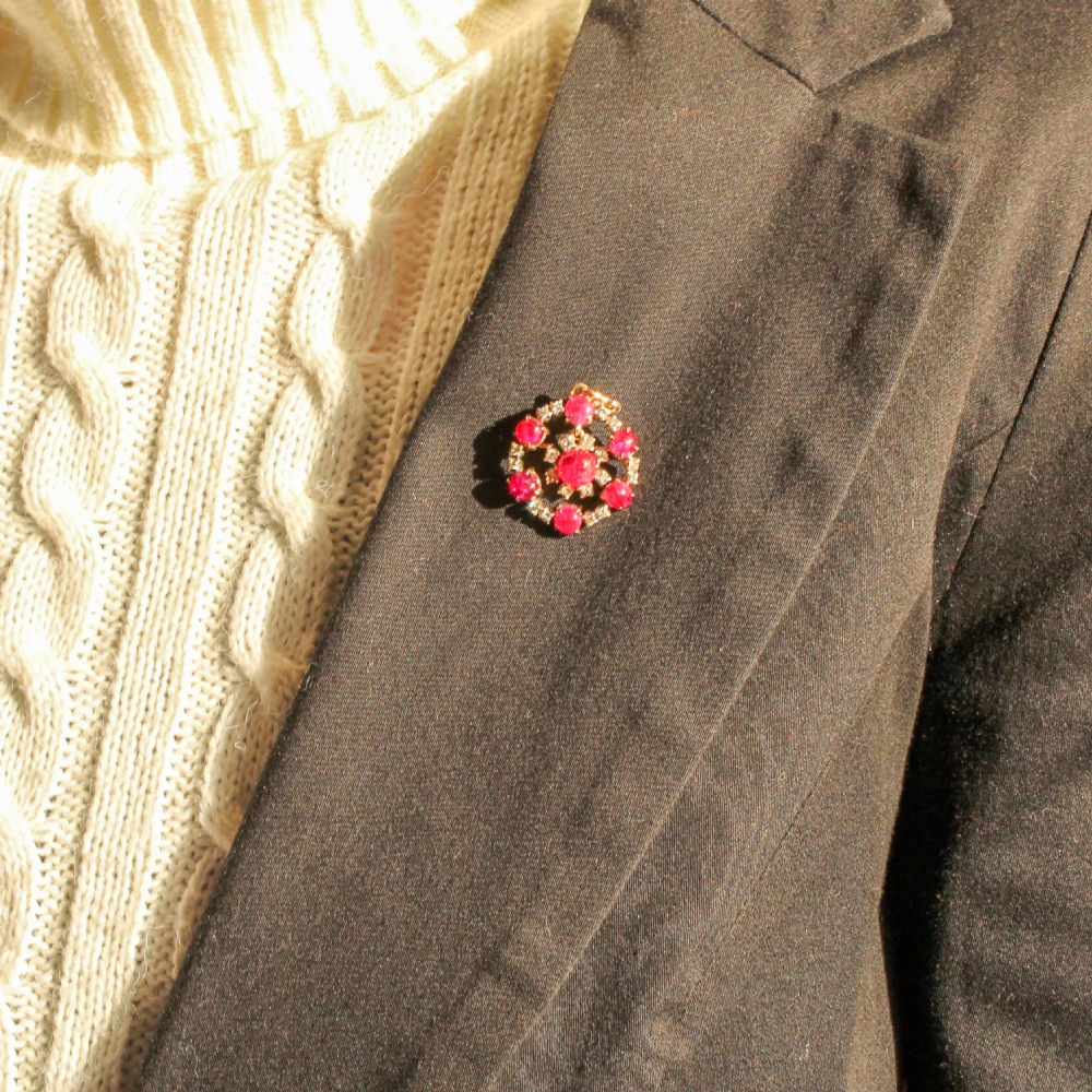 A late Victorian circular pendant brooch set with cabochon rubies framed by diamond halos, suspended from a fine silver chain. View II