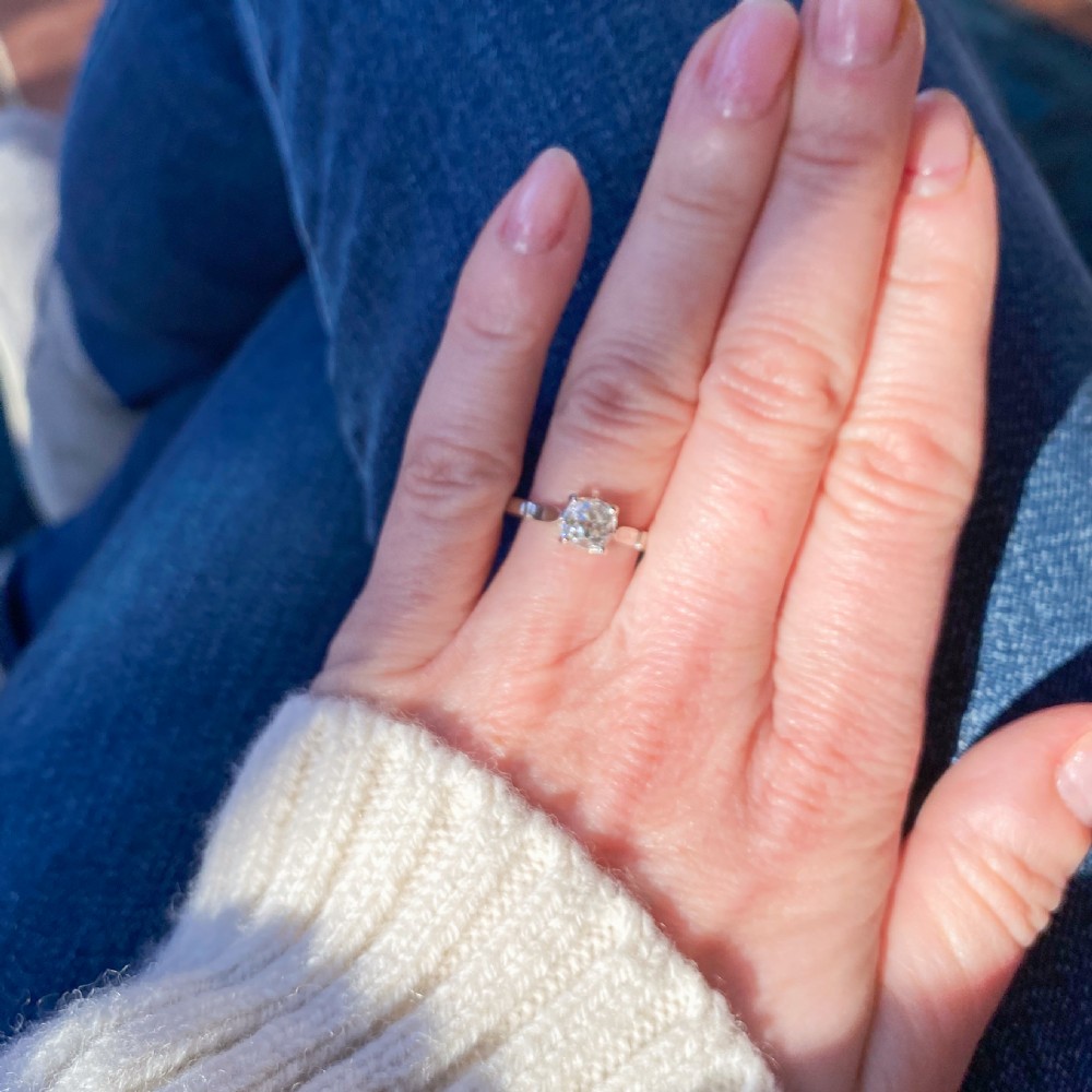 An Art Deco diamond solitaire engagement ring featuring a single old-cut diamond set in a four-prong setting with geometric shoulder detail on a silver-tone band. View VII