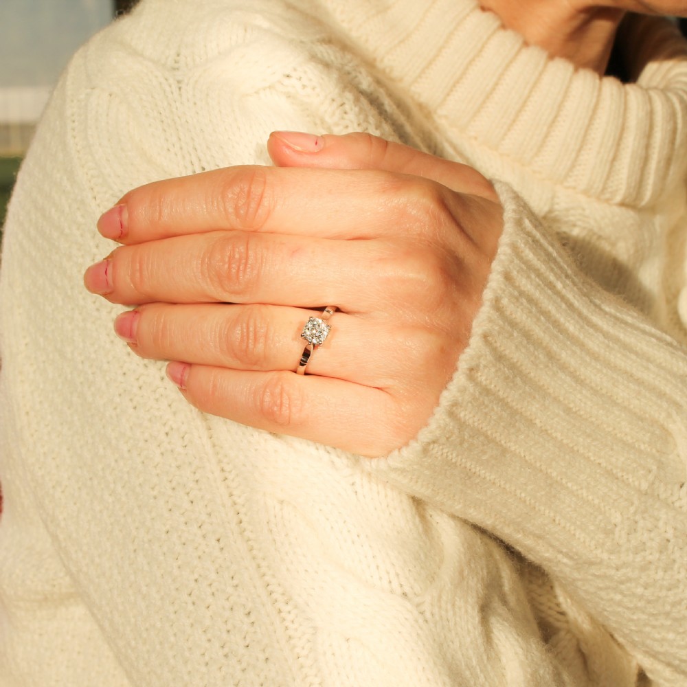 An Art Deco diamond solitaire engagement ring featuring a single old-cut diamond set in a four-prong setting with geometric shoulder detail on a silver-tone band. View VIII