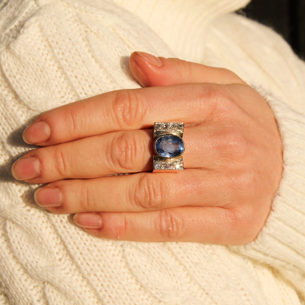 A mid-century gold ring featuring a central oval blue sapphire set in a wide band with diamond-set vertical shoulders. View II