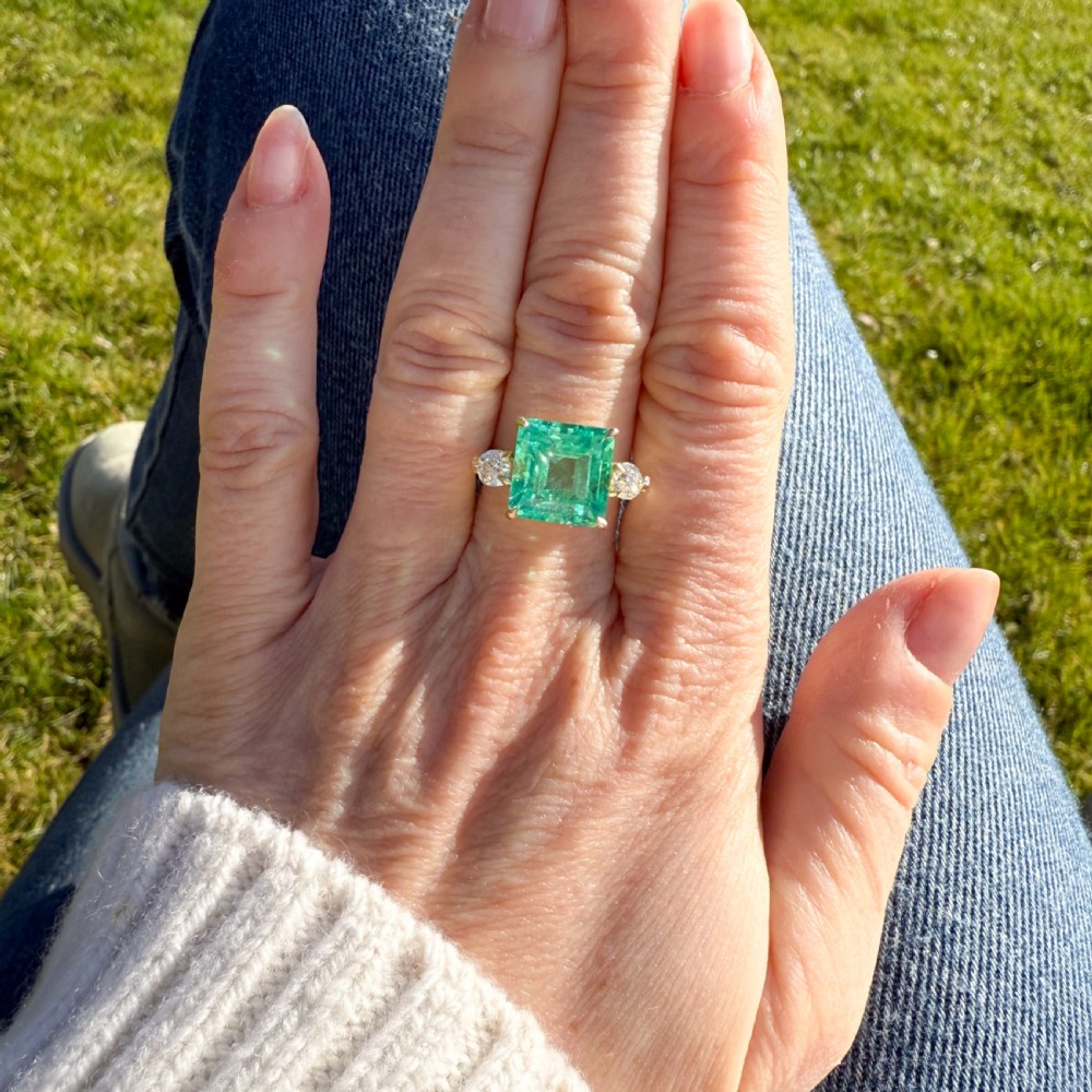 An Edwardian yellow gold trilogy ring set with a large square step-cut green emerald flanked by two round diamonds. View VI