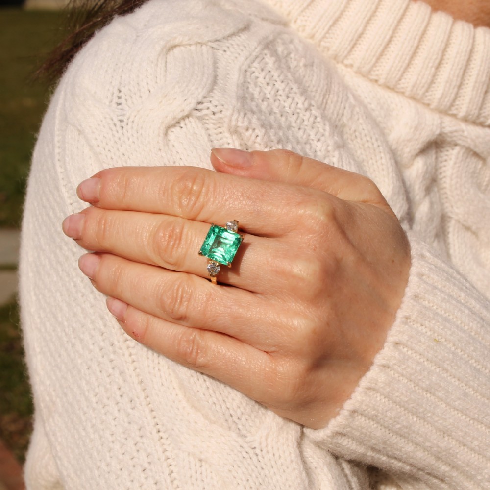 An Edwardian yellow gold trilogy ring set with a large square step-cut green emerald flanked by two round diamonds. View VII