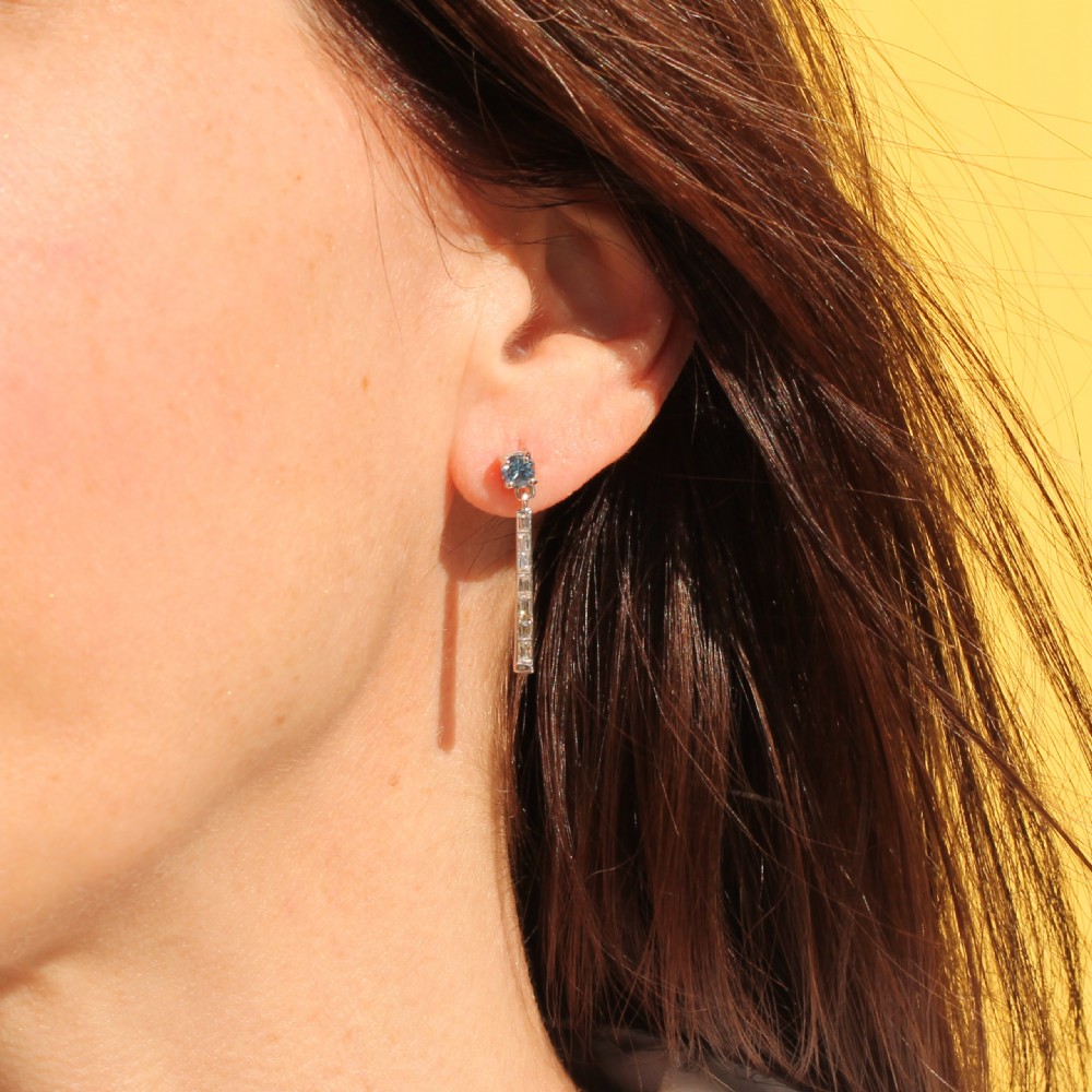 A pair of mid-century platinum drop earrings featuring round light-blue aquamarines above vertical bars set with baguette-cut diamonds. View VI