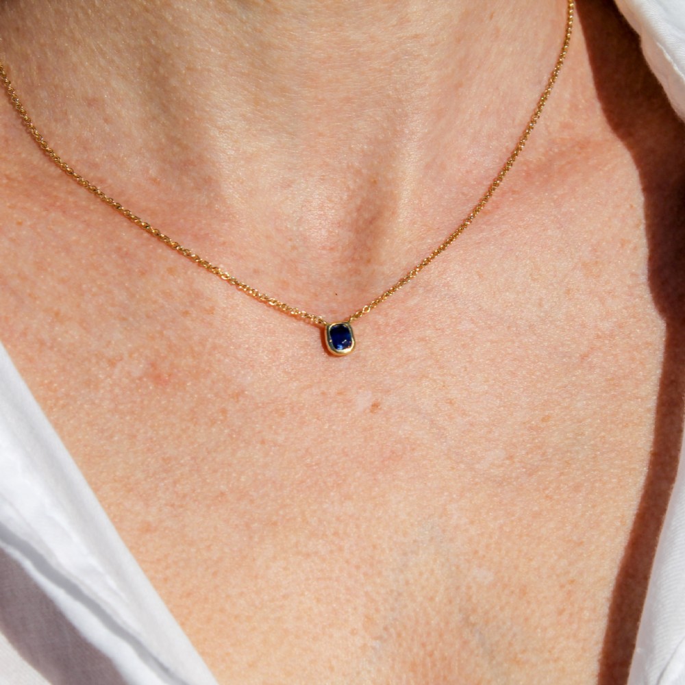An Art Deco yellow gold necklace showcasing a central cushion-cut blue sapphire solitaire in a rub-over setting attached to a thin trace chain. View III