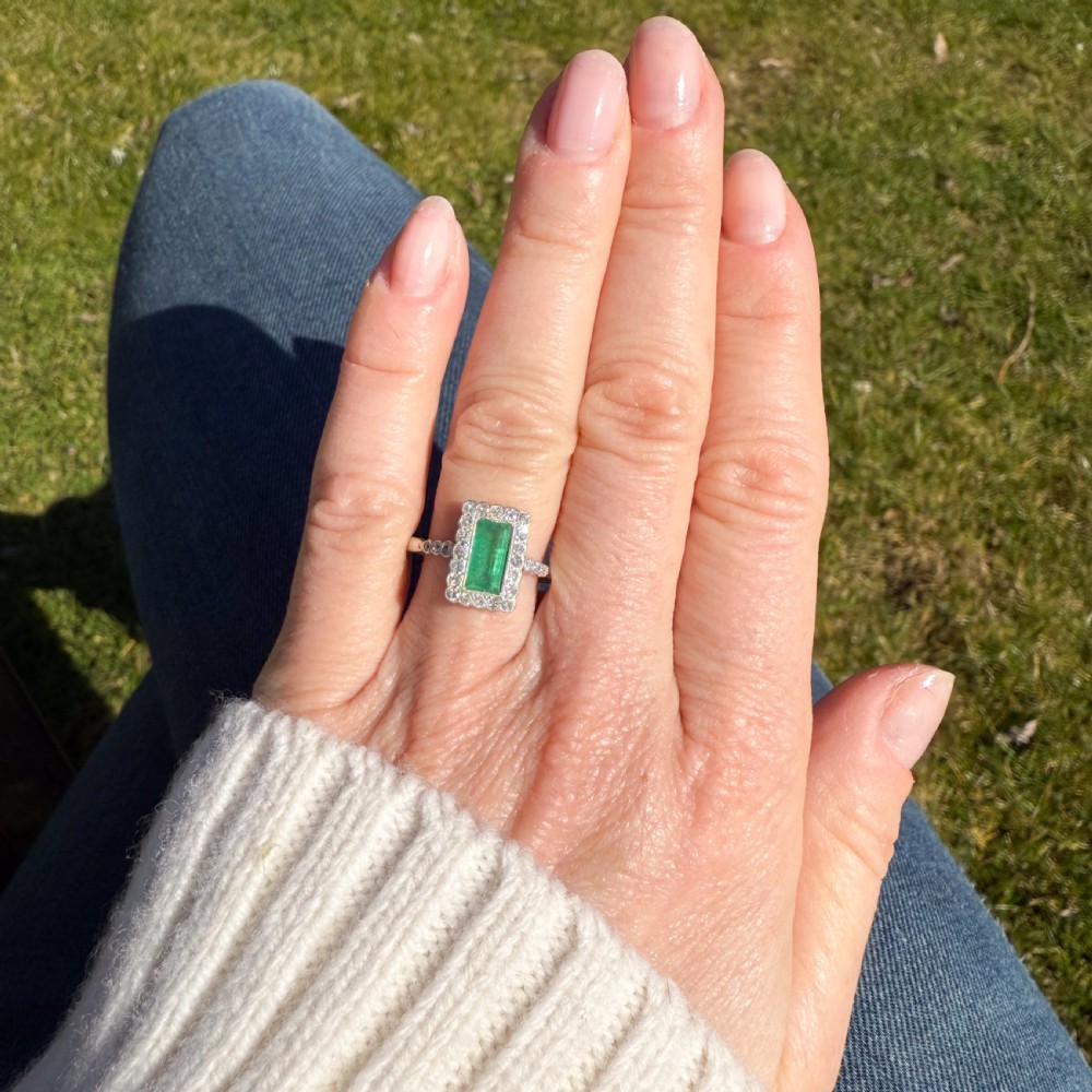 A mid-century rectangular emerald cluster ring set in white metal, bordered by small round diamonds with a detailed band. View VI