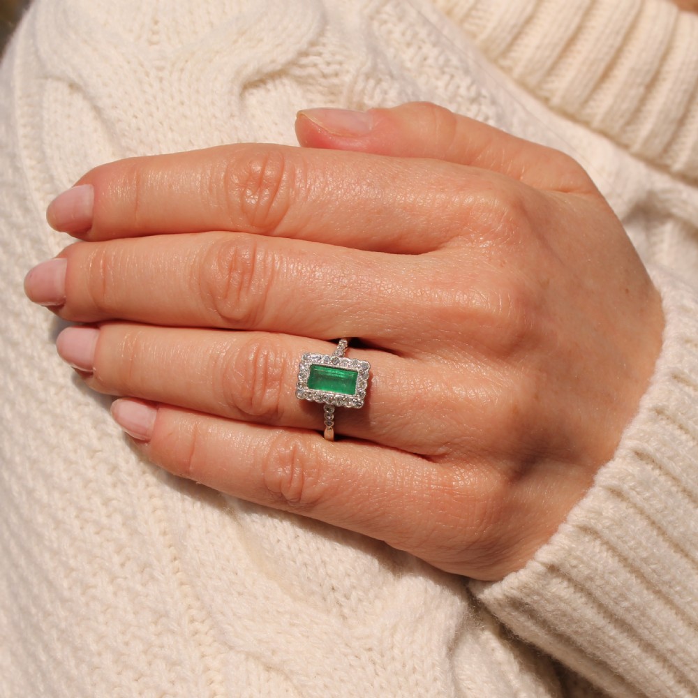 A mid-century rectangular emerald cluster ring set in white metal, bordered by small round diamonds with a detailed band. View VII