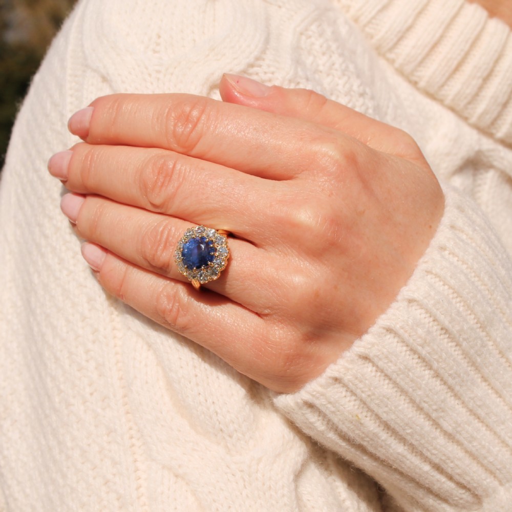 An Edwardian period cluster ring crafted in yellow gold featuring a large round blue Ceylon sapphire surrounded by a halo of white diamonds in claw settings. View II