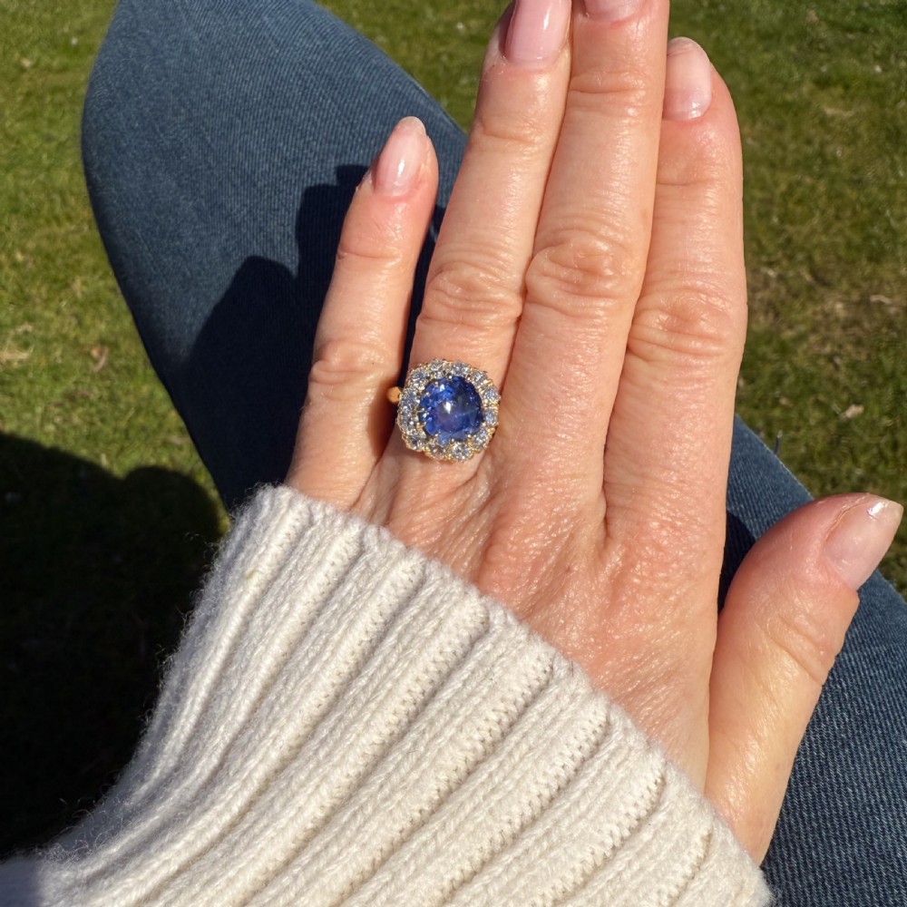An Edwardian period cluster ring crafted in yellow gold featuring a large round blue Ceylon sapphire surrounded by a halo of white diamonds in claw settings. View VI