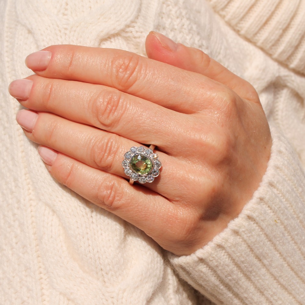 An Art Deco ring featuring an oval yellow-green chrysoberyl gemstone encircled by a halo of round diamonds set in platinum. View VII