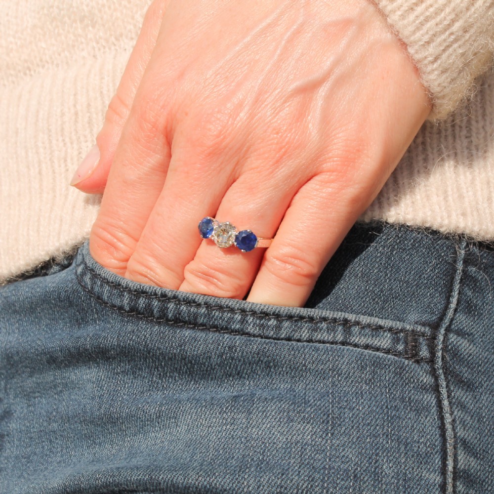 An Art Deco trilogy ring featuring a central old cut diamond flanked by two round blue sapphires set in platinum claws on a yellow gold band. View II