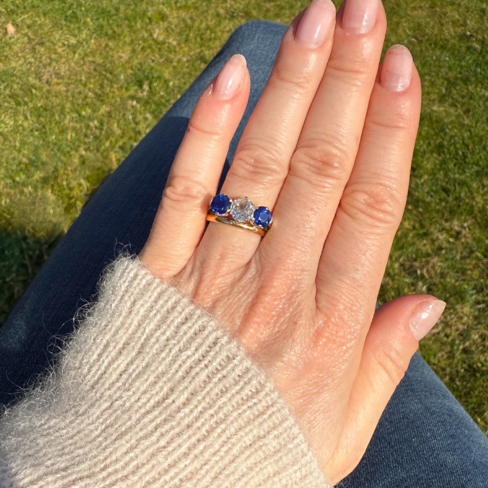 An Art Deco trilogy ring featuring a central old cut diamond flanked by two round blue sapphires set in platinum claws on a yellow gold band. View VI