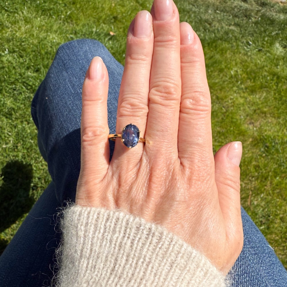 A mid-century yellow gold solitaire ring featuring a large oval cut blue sapphire in a six-prong basket setting. View VI