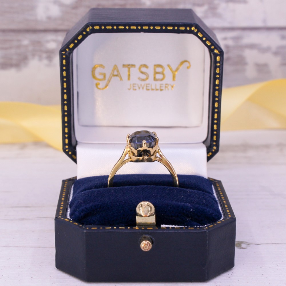 A mid-century yellow gold solitaire ring featuring a large oval cut blue sapphire in a six-prong basket setting. View IX